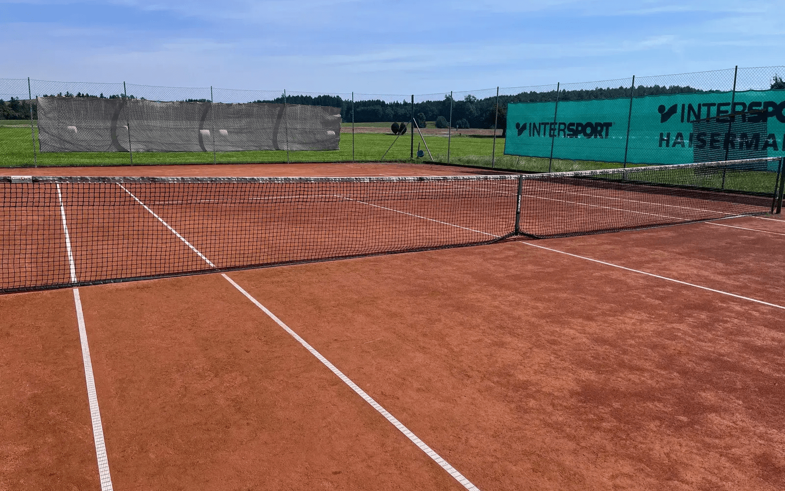 Tennissandplatz mit Netz, Linien und Windfang